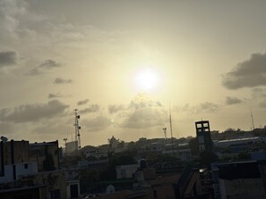 Un paisaje urbano con edificios, una torre destacada y el sol poniéndose o saliendo en el cielo.