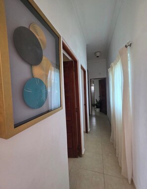 Un pasillo con una obra de arte enmarcada, una puerta y vista a otra habitación.