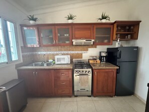 Una cocina con gabinetes de madera, microondas, estufa, refrigerador y cafetera.
