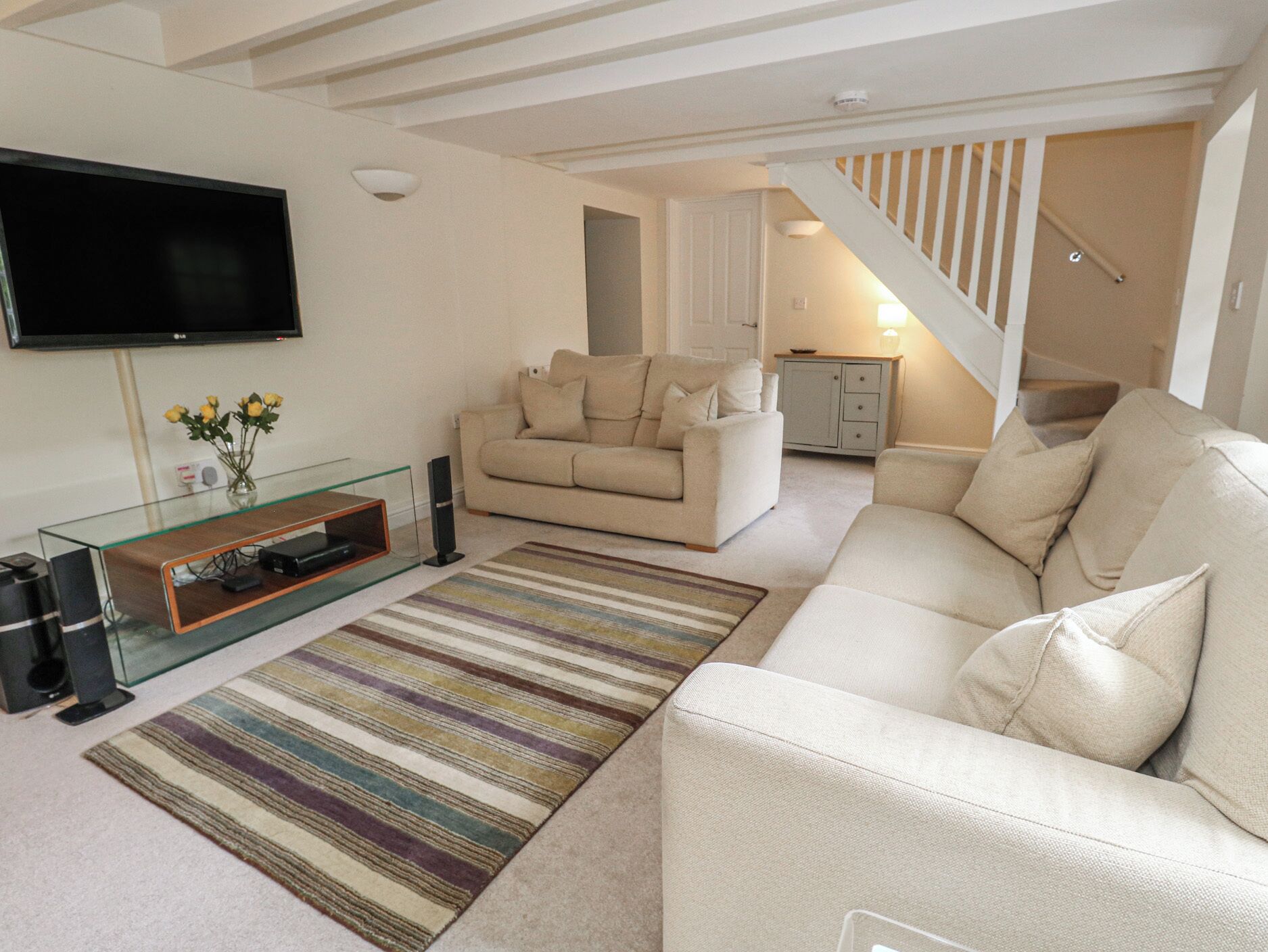 A living room with a sofa, a glass coffee table, a flat-screen TV, and a striped rug.