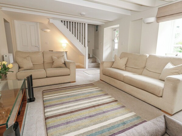 A living room with two beige sofas, a striped rug, and a staircase.