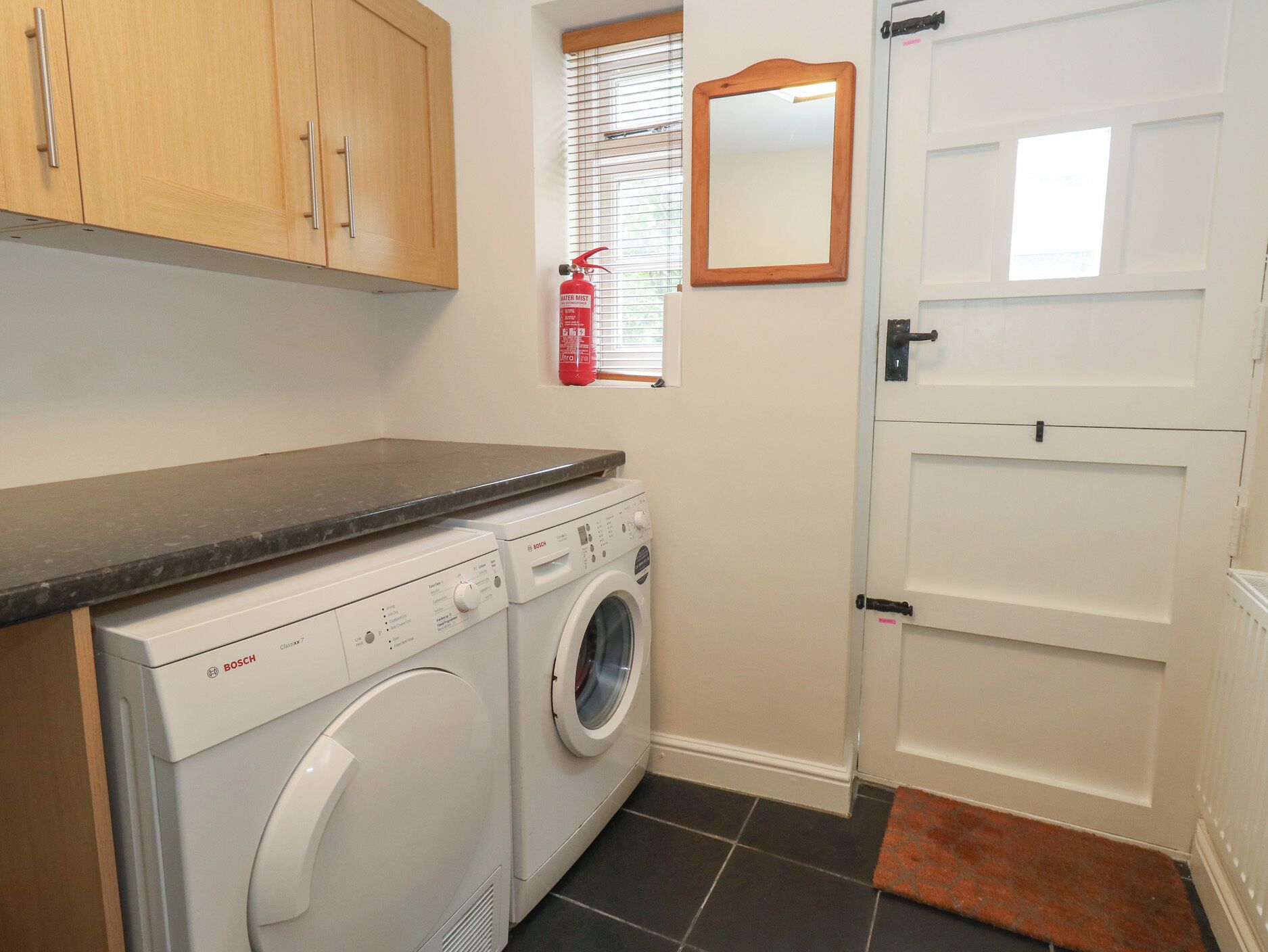 A laundry area with a Bosch washing machine, a fire extinguisher, and a door with a handle.