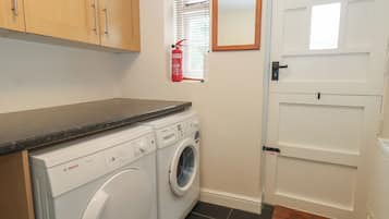 A laundry area with a Bosch washing machine, a fire extinguisher, and a door with a handle.