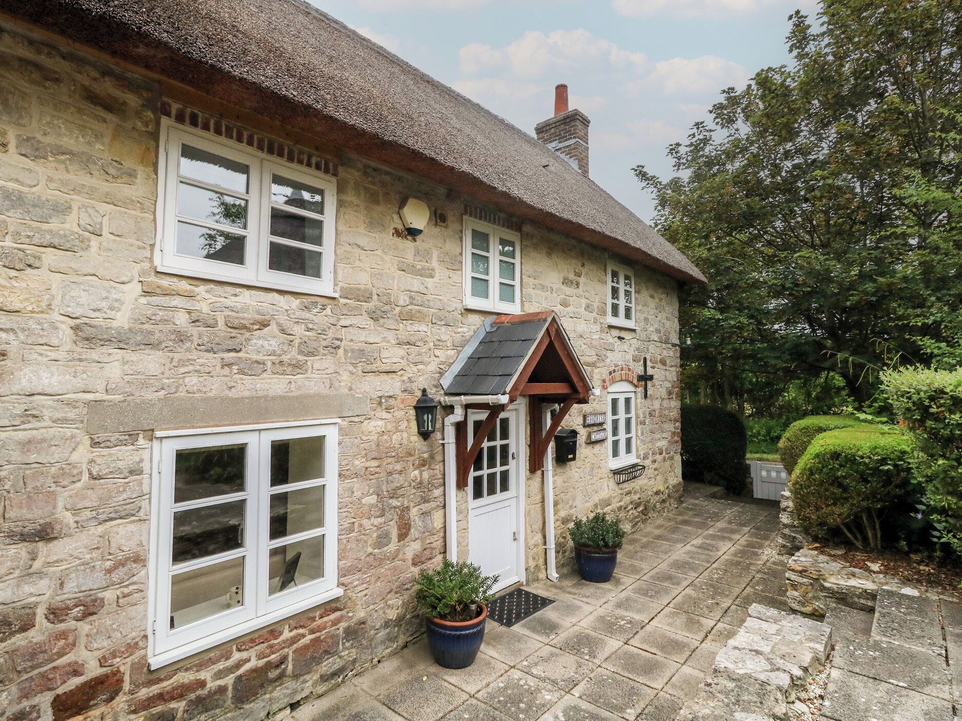 A stone house with a thatched roof, a wooden door, and a small garden with potted plants.