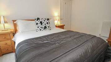 Un dormitorio con una cama, dos mesitas de noche, una lámpara, una puerta y un radiador.