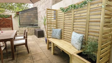 An outdoor patio with a wooden bench, a table, and chairs.