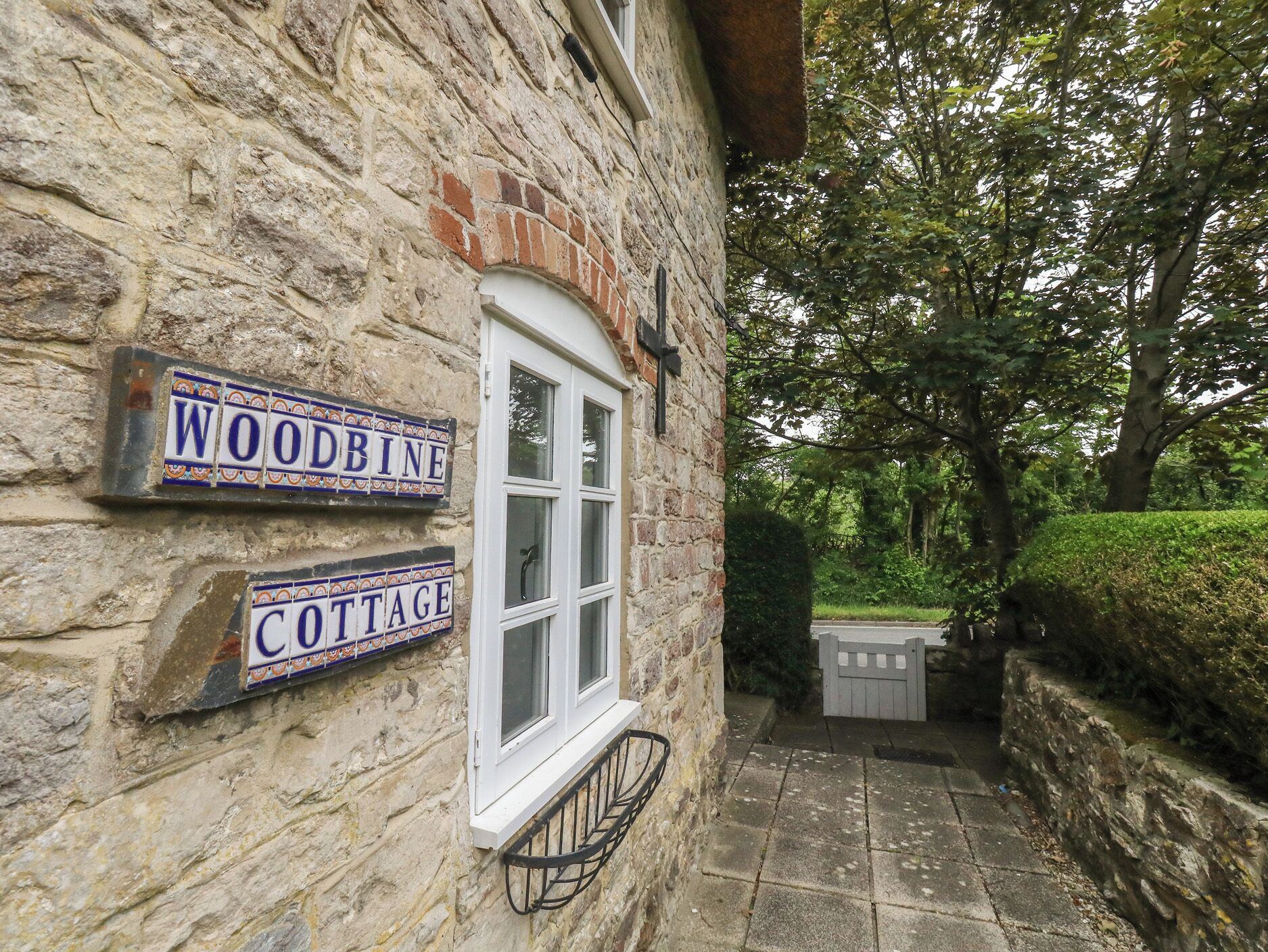 A stone cottage with a window and two signs reading 'WOODBINE' and 'COTTAGE'.