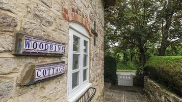 A stone cottage with a window and two signs reading 'WOODBINE' and 'COTTAGE'.