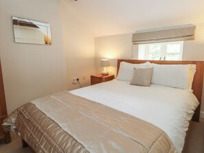 Uma cama bem arrumada com cabeceira, luminária de cabeceira e janela com cortinas.