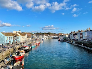 A harbor with boats docked along the waterfront, buildings lining the shore, and a clear blue sky. - Woodbine Cottage (Weymouth)