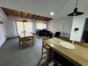 A modern interior with a wooden dining table, a sofa, and a ceiling with exposed beams.
