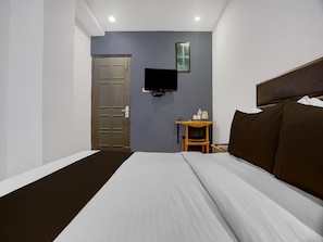 Ein Hotelzimmer mit Bett, Wandfernseher, einem kleinen Holztisch und einer Tür.