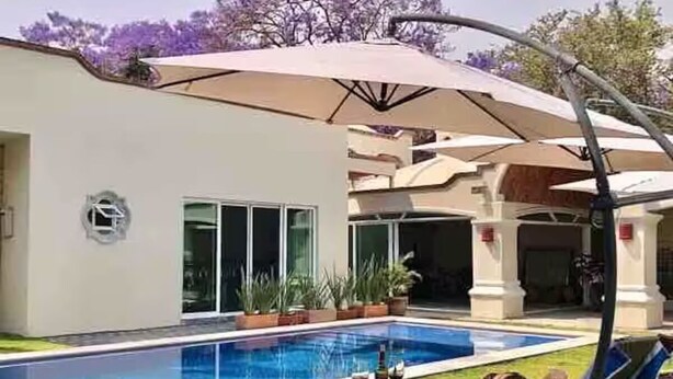 A swimming pool with lounge chairs and umbrellas, surrounded by a modern building with large windows and a covered patio area.