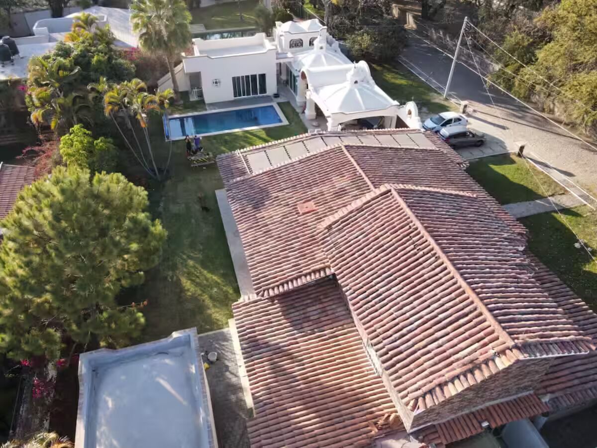 Il s’agit d’une propriété résidentielle dotée d’une piscine, d’un grand jardin et d’une maison blanche avec un toit recouvert de tuiles rouges.