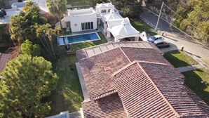 A residential property with a swimming pool, a large garden, and a white house with a red-tiled roof.