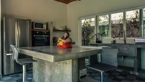 A modern kitchen with a large island, stainless steel appliances, and a view through large windows.