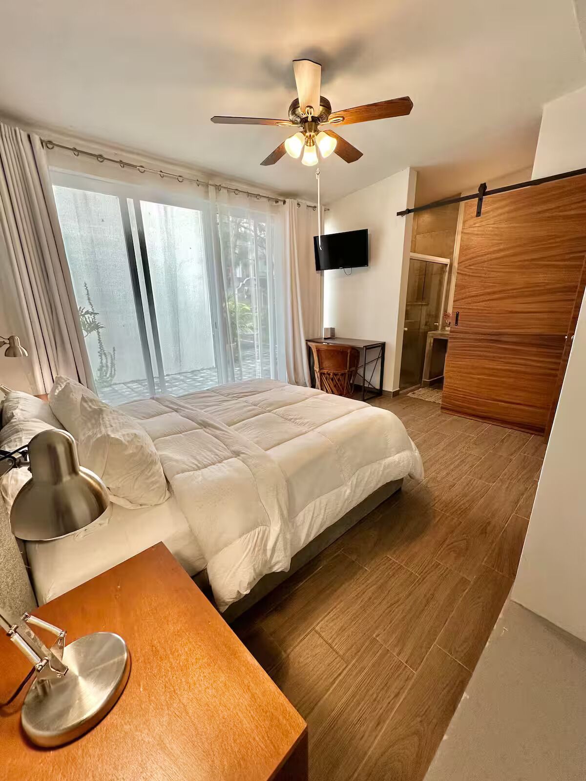 Une chambre à coucher comprenant un lit, un bureau, une chaise, un ventilateur de plafond, une télévision et une porte coulissante.