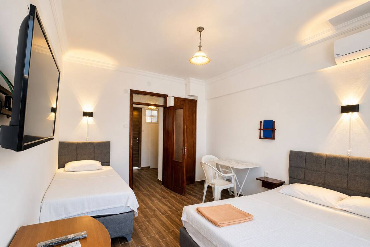 Habitació d'hotel amb dos llits, un escriptori, una cadira, un televisor i una làmpada al sostre.