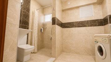 A bathroom with a shower, toilet, and washing machine.