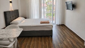 Una camera da letto con un letto, una scrivania, una sedia, una TV e una finestra con tende.