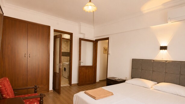 Una camera d'albergo con un letto, una scrivania, una sedia, un armadio e una lavatrice sullo sfondo.