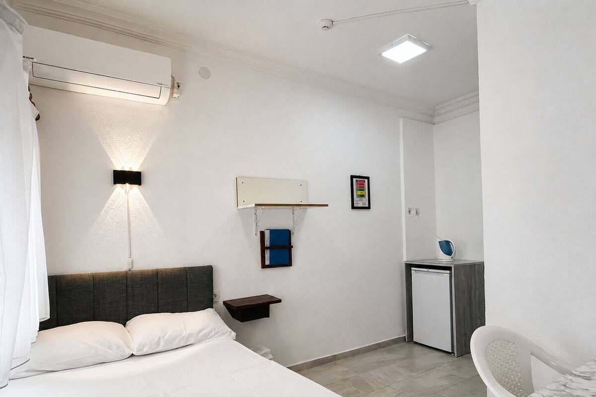 Habitació d'hotel amb llit, taulell de nit, làmpada i escriptori petit amb cadira.