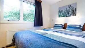 Un dormitorio con dos camas, un radiador, una ventana con cortinas y un cuadro de un cactus en la pared.