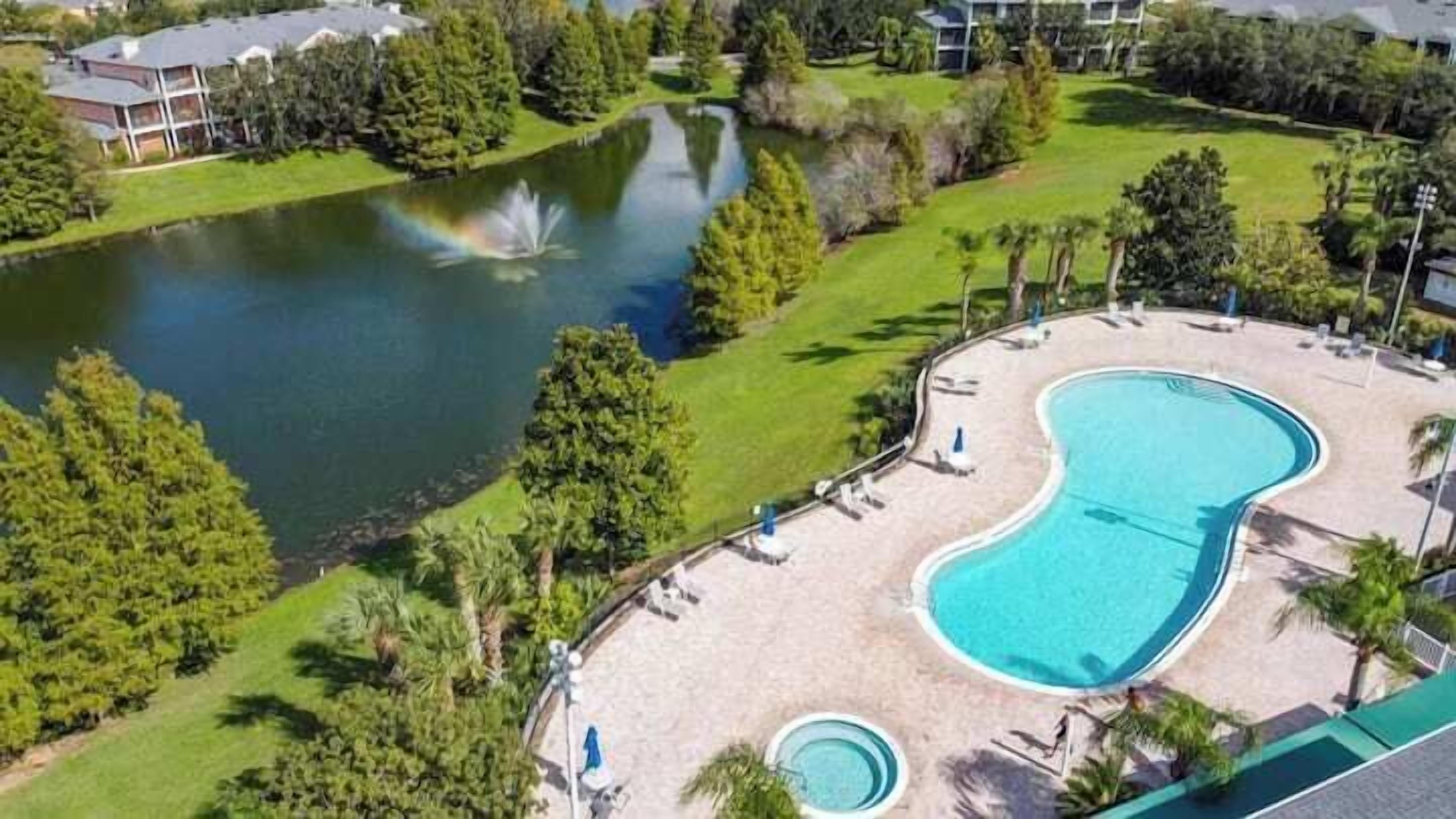 A swimming pool with a fountain, surrounded by a deck with lounge chairs and a lawn area with a pond.