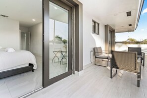 Ein modernes Schlafzimmer mit einem Bett, einer Glastür, die auf einen Balkon führt, und einer Sitzecke mit Stühlen.