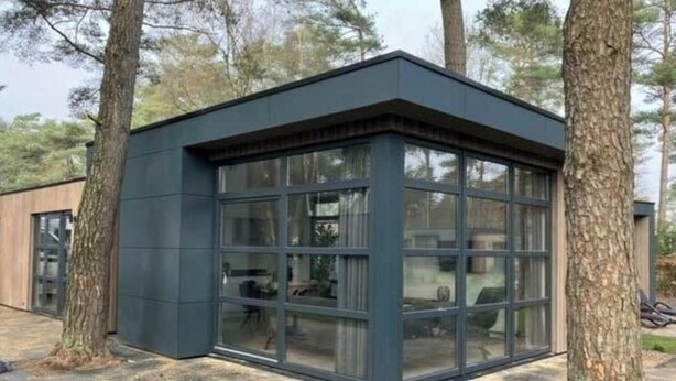 Una estructura moderna con paredes de vidrio y exterior oscuro, rodeada de árboles.