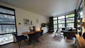 Amplia sala de estar con mesa de comedor, sofás y ventanas grandes que ofrecen vistas al exterior.