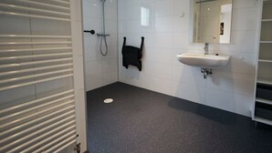 Un baño con paredes de azulejos blancos, suelo negro moteado, un lavamanos blanco, una ducha de mano y un perchero para toallas.