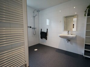 Ein Badezimmer mit weißen Fliesenwänden, einem schwarz gefleckten Boden, einem weißen Waschbecken, einer Duschbrause und einem Handtuchhalter.