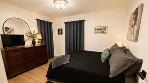 A bedroom with a bed, a dresser, a TV, and a chandelier.