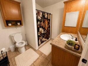 Un baño con inodoro, lavamanos, cortina de ducha y armarios de madera.