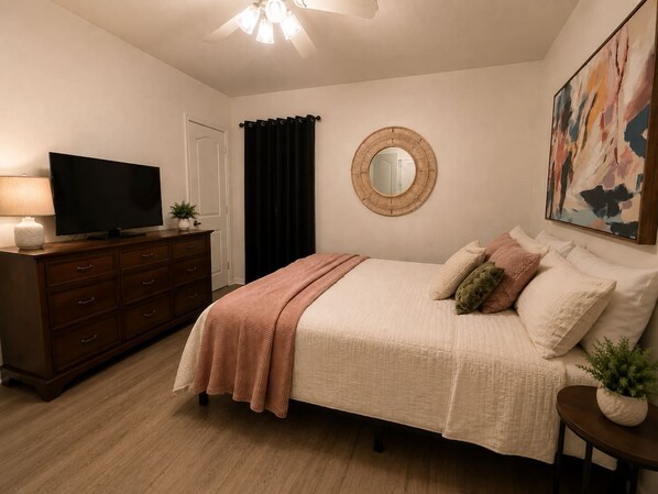 A bedroom with a bed, dresser, television, and artwork.
