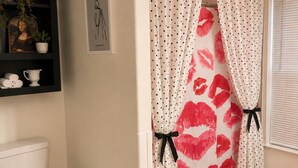 A bathroom with a toilet, a shelf with decorative items, a framed picture, and a shower curtain with a polka dot pattern.