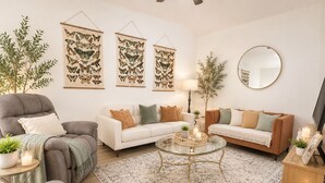 A living room with a grey armchair, white sofas, a glass coffee table, and wall-mounted butterfly art.