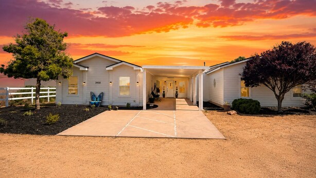 A two-story mobile home with a covered driveway and a fenced yard.
