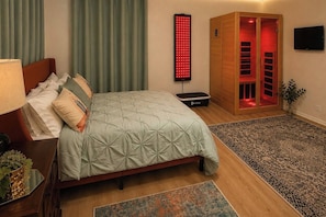 A bedroom with a bed, a massage chair, a red light panel, a wooden cabinet, and a TV.