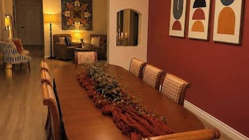 Uma sala de jantar com uma longa mesa de madeira, cadeiras, um candelabro e obras de arte nas paredes.