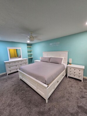 A bedroom with a bed, two nightstands, a dresser, a ceiling fan, and a wall with a motivational quote.