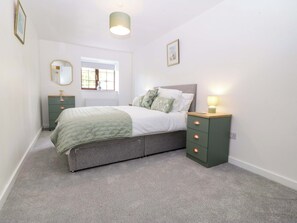 Un dormitorio con cama, mesitas de noche, ventana y lámpara.