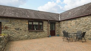 A stone building with a tiled patio, a door, and a window. - Cil Y Coed (Gaerwen)
