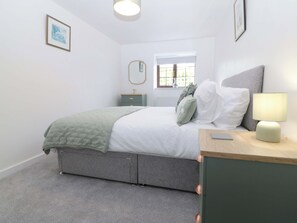 A bedroom with a bed, bedside table, lamp, dresser, and a window with a view.