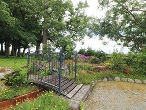 Un jardín con un puente de madera, una valla metálica y diversas plantas y flores.