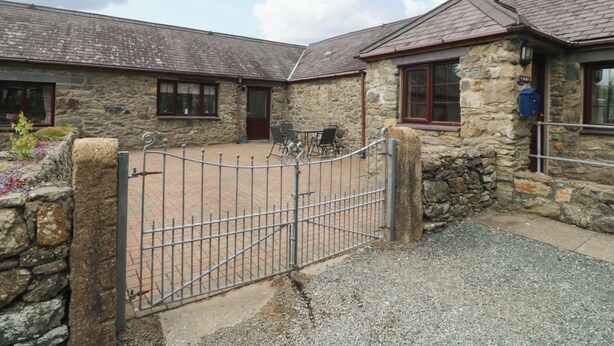 A stone building with a metal gate, a window with a red frame, and a mailbox. - Cil Y Coed (Gaerwen)