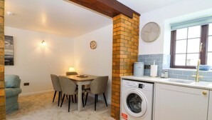 A compact kitchen with a washing machine, a dining area with chairs, a clock, and a window with a view. - Cil Y Coed (Gaerwen)