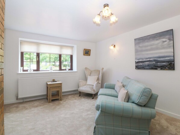 A room with a window, a radiator, a small table, a chair, a sofa, and a painting on the wall.