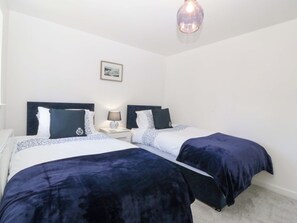 Habitación doble con dos camas, una mesita de noche con lámpara, un cuadro enmarcado en la pared y una lámpara colgante.